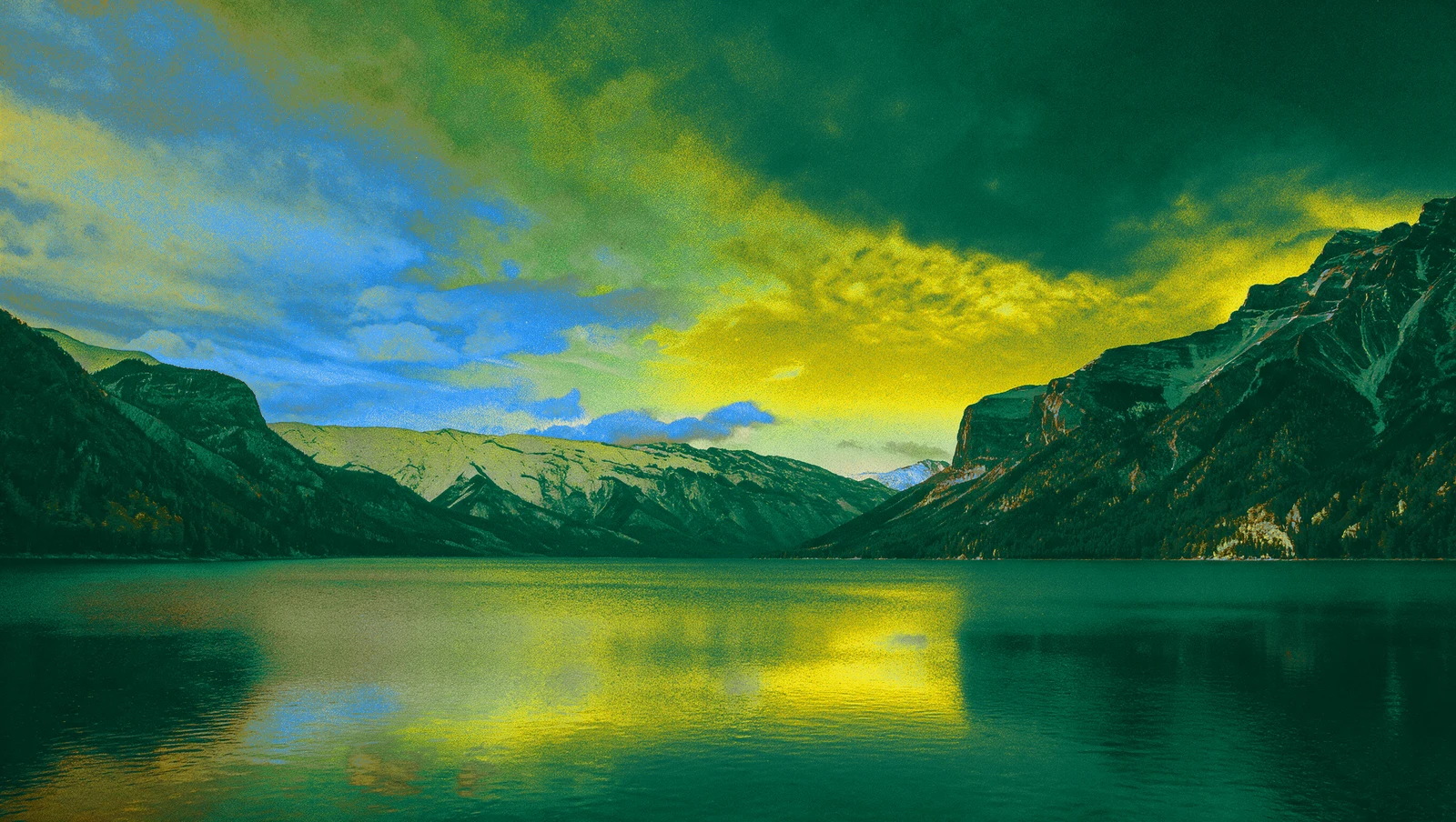 A mountain lake reflecting a blue, gold and green sky.
